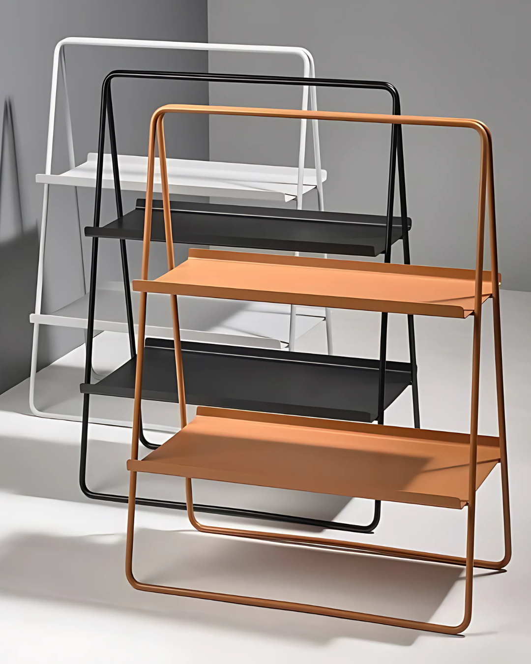 A minimalist light gray & orange & Black display A-Table leans against a white wall, showcasing its simple and elegant design. The table features two rectangular shelves supported by an A-shaped frame made of slender, rounded metal. Its open structure and clean lines create a light and airy feel