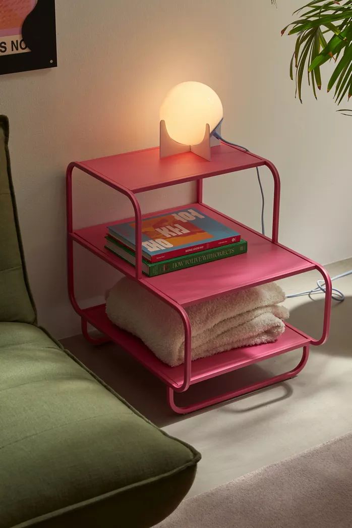 Pink color Alana Nightstand with two shelves, displaying a clock, radio, vase, and figurines. Modern shelving unit.