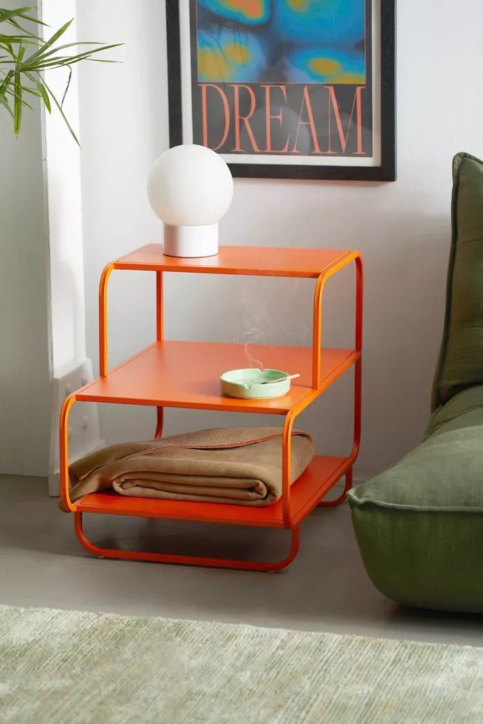 orange Alana Nightstand with two shelves, displaying a clock, radio, vase, and figurines. Modern shelving unit.