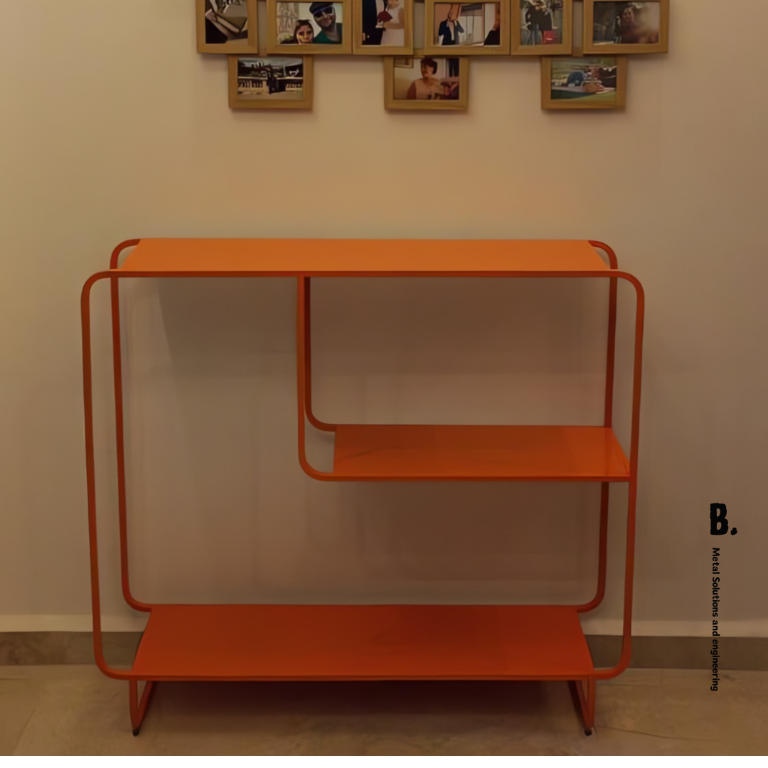 The Alana console, an orange color metal table with shelves, showing a vase, books, and a speaker.