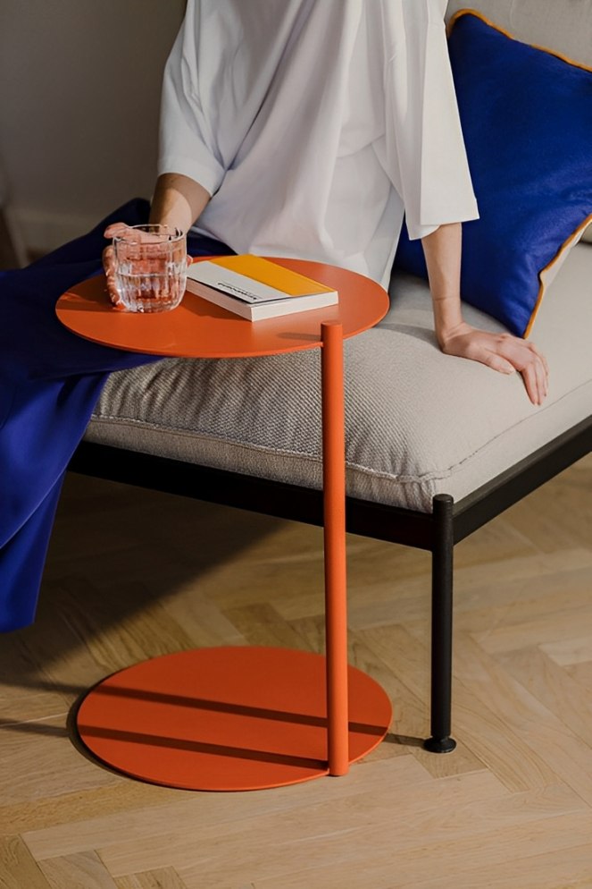 Orange side table with two round tiers connected by a vertical stem, resting on a light wood floor.