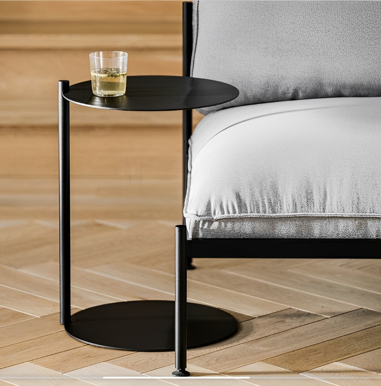 Black side table with two round tiers connected by a vertical stem, resting on a light wood floor.