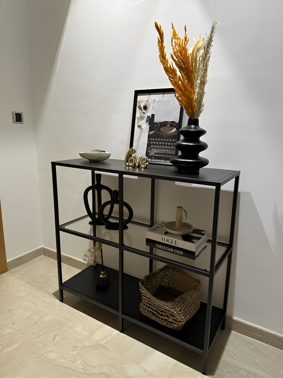 Modern industrial style shelving unit with a thin black metal frame and clear glass tiers.