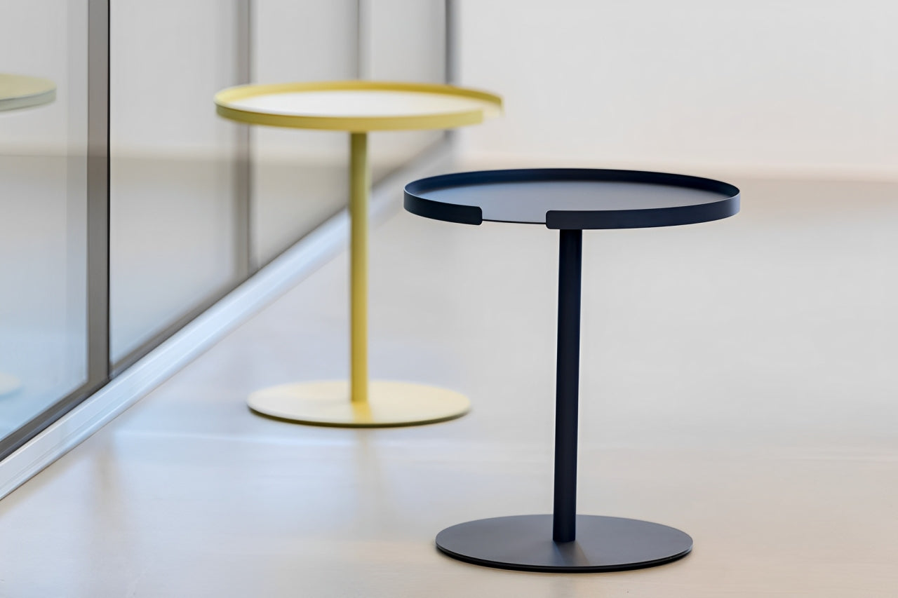 Two contemporary side tables, one yellow with a white tabletop, the other black, both with round tops and bases, on a light, reflective surface.