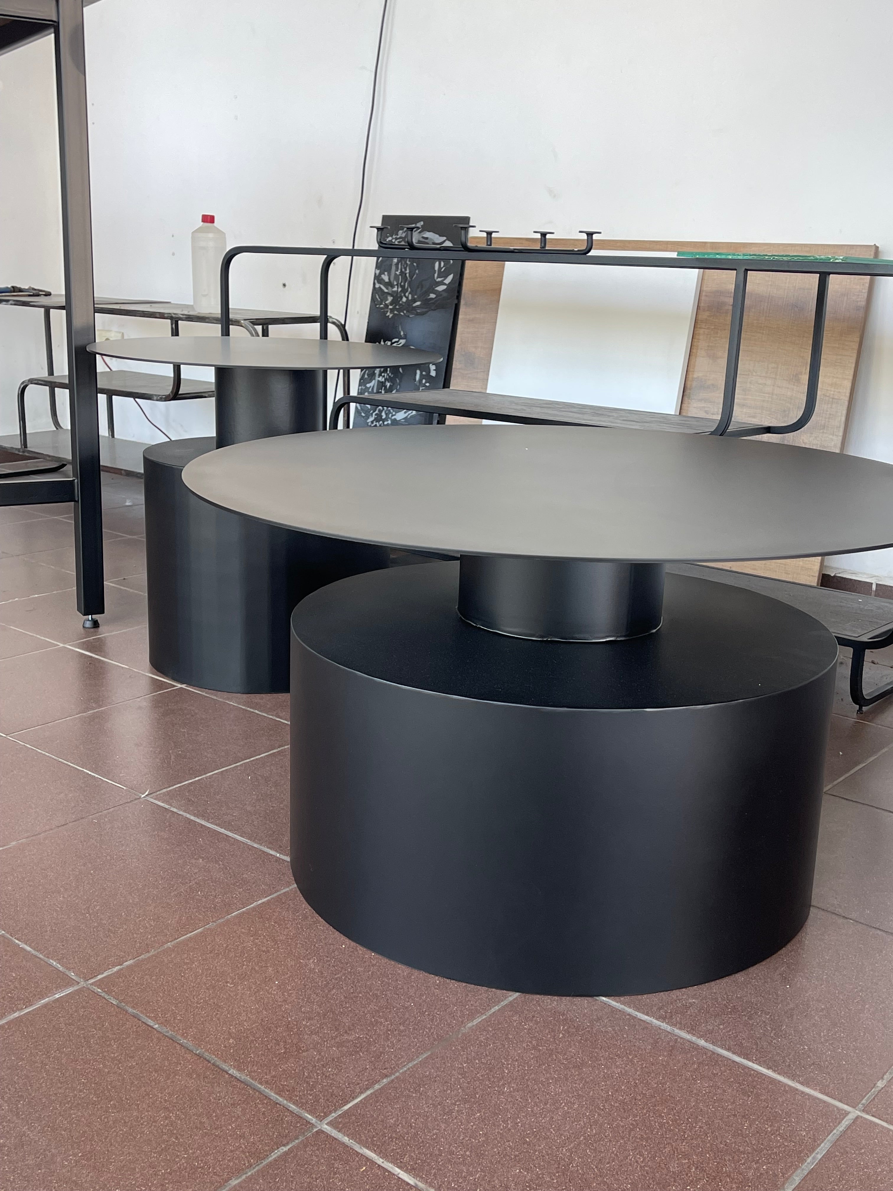 Modern nesting coffee tables with geometric shapes, featuring black metal oval and round tops and cylindrical bases.