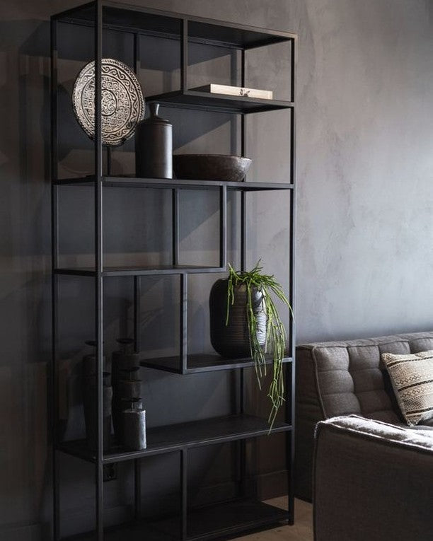 Modern black metal bookshelf with open, asymmetrical shelving. Displaying decorative plates, vases, plants, and books. Contemporary design for home or office storage and display.