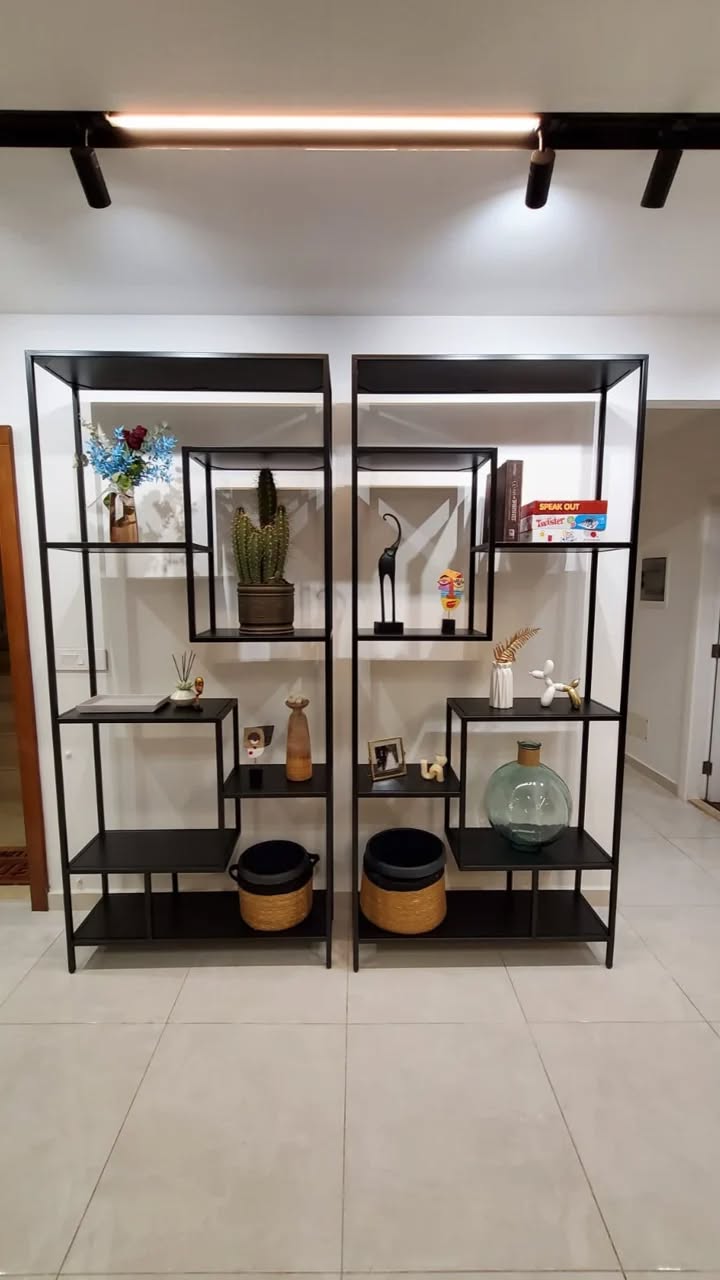 Modern black metal bookshelf with open, asymmetrical shelving. Displaying decorative plates, vases, plants, and books. Contemporary design for home or office storage and display.