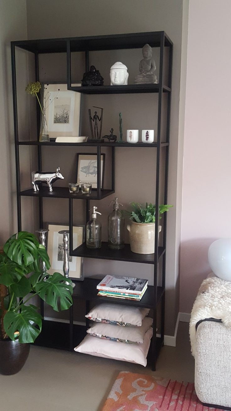 Modern black metal bookshelf with open, asymmetrical shelving. Displaying decorative plates, vases, plants, and books. Contemporary design for home or office storage and display.