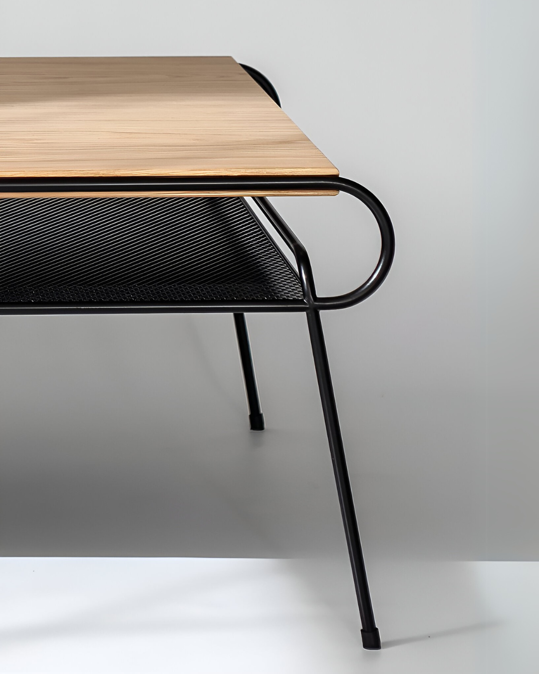 Close-up of HAY Mags Coffee Table. Detail of light wood tabletop, curved black metal frame, and black perforated metal shelf.