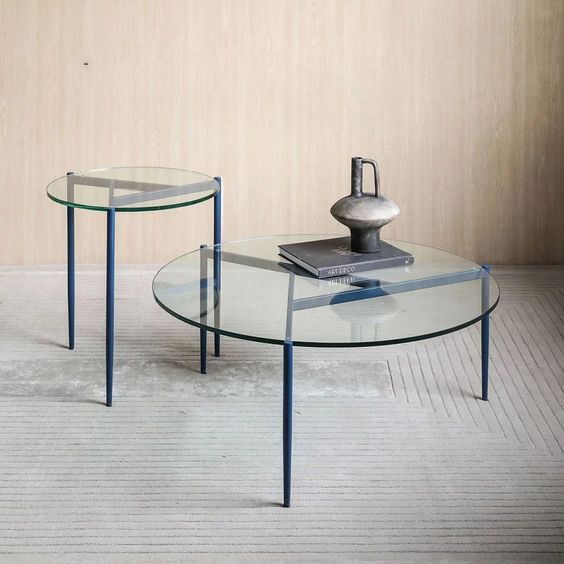 Halo set table set of two round nesting tables with glass tops and blue metal frames, on a light-colored floor.