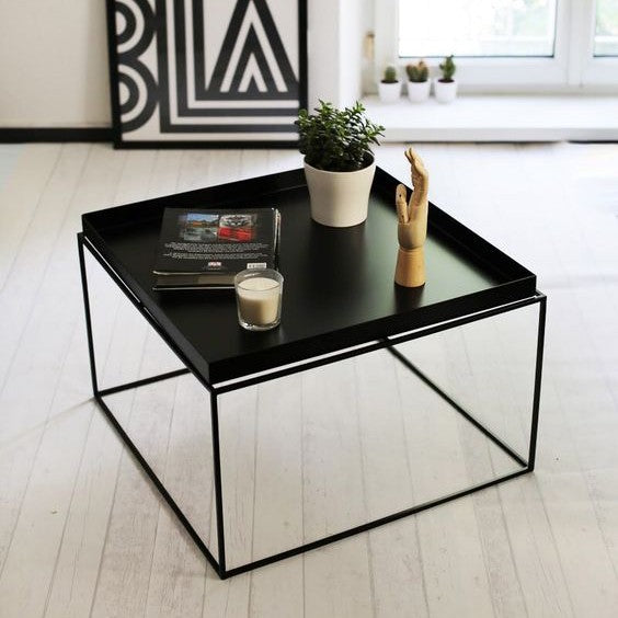 Modern black square tray table, minimalist metal frame, styled with book, candle, plant, and wooden hand.