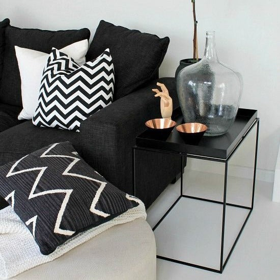 Black metal tray table, square design, styled with glass vase and copper bowls in a modern living room setting with a black sofa and patterned pillows