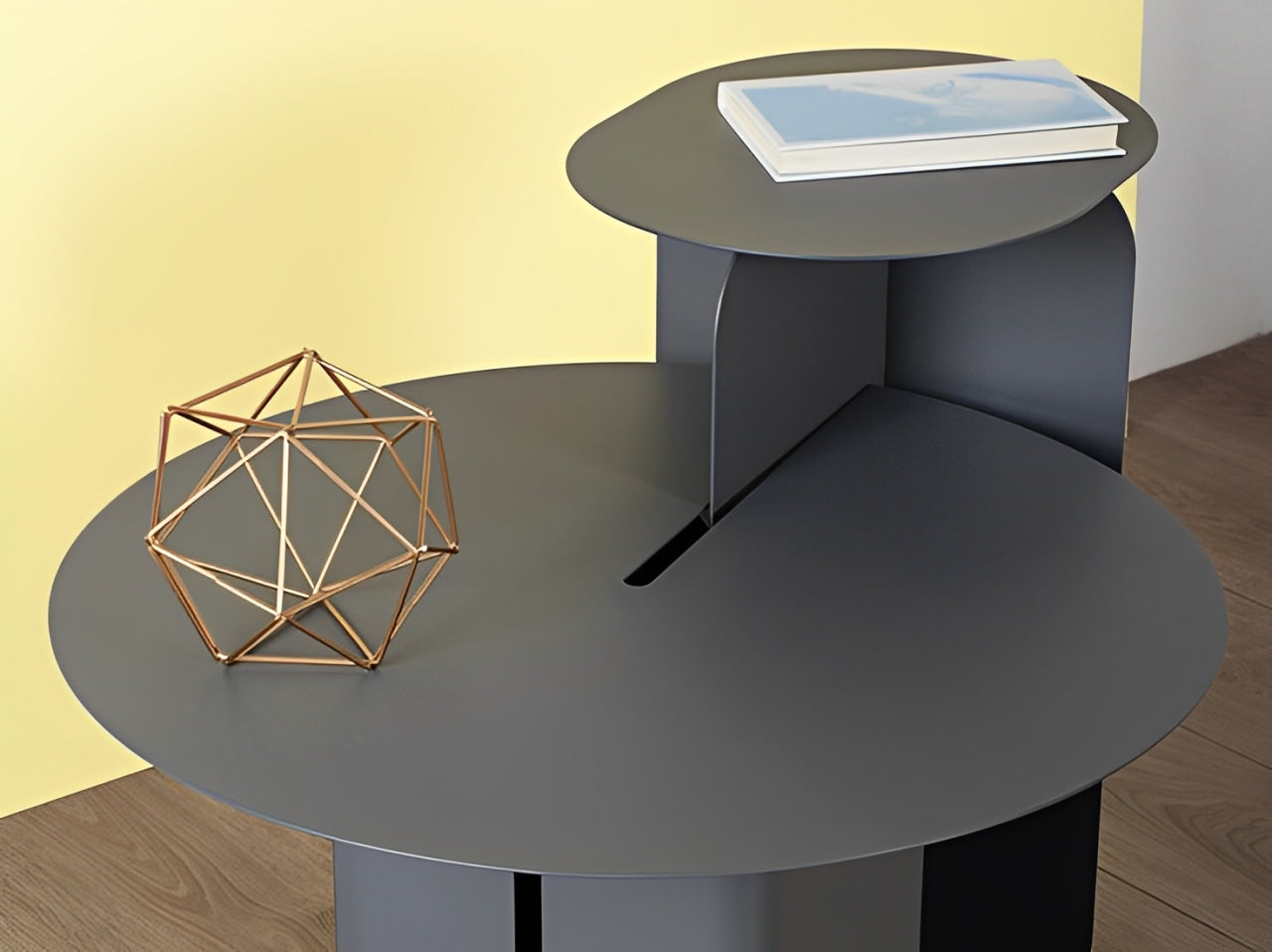 Modern gray round side table with tiered design, gold geometric sculpture, and book.