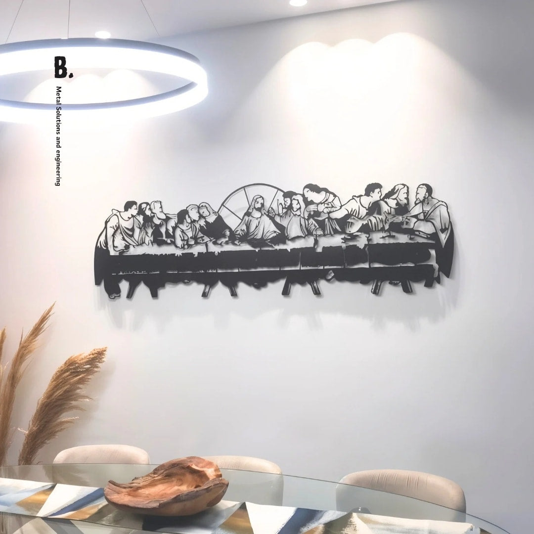 A detailed black metal silhouette of the Last Supper, showing Jesus and his disciples at a long table, mounted on a white wall. The artwork is cut out in a stylized, modern way.
