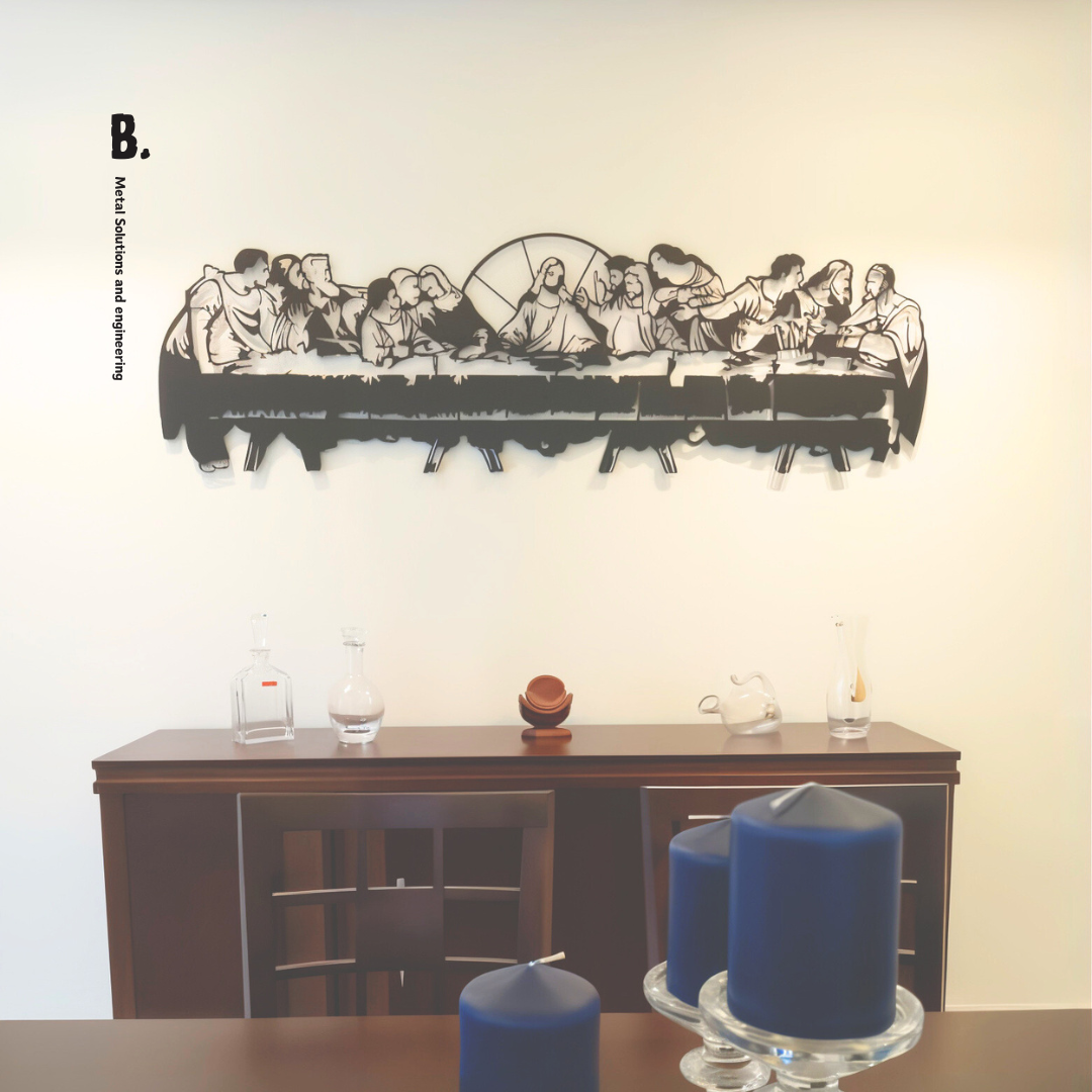 A detailed black metal silhouette of the Last Supper, showing Jesus and his disciples at a long table, mounted on a white wall. The artwork is cut out in a stylized, modern way.