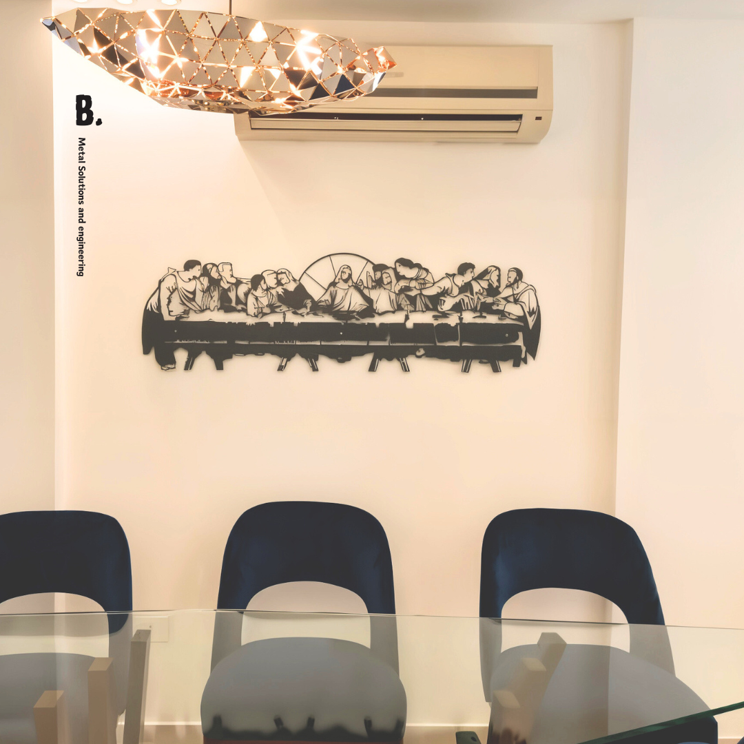 A detailed black metal silhouette of the Last Supper, showing Jesus and his disciples at a long table, mounted on a white wall. The artwork is cut out in a stylized, modern way.