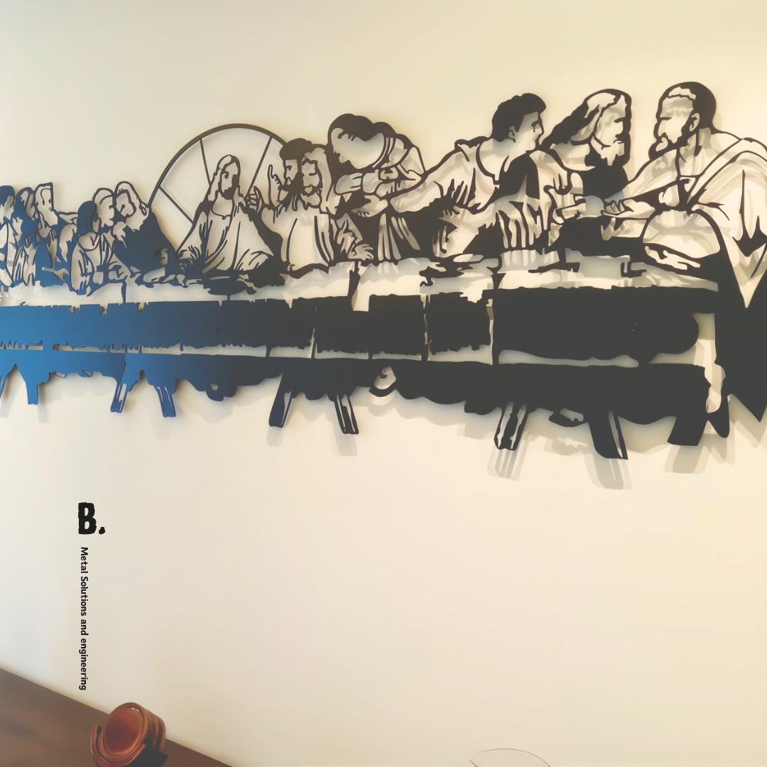 A detailed black metal silhouette of the Last Supper, showing Jesus and his disciples at a long table, mounted on a white wall. The artwork is cut out in a stylized, modern way.