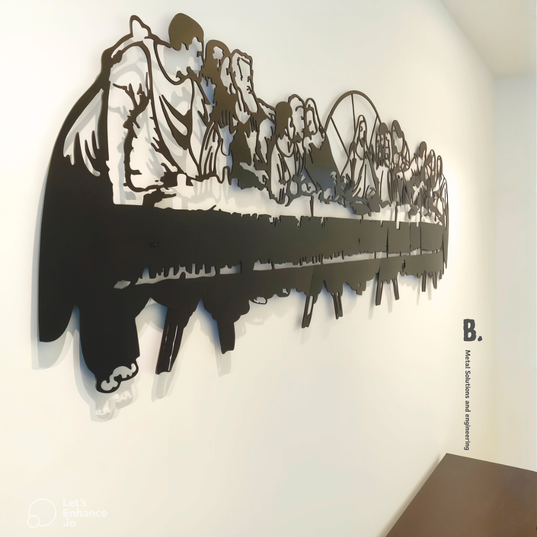 A detailed black metal silhouette of the Last Supper, showing Jesus and his disciples at a long table, mounted on a white wall. The artwork is cut out in a stylized, modern way.
