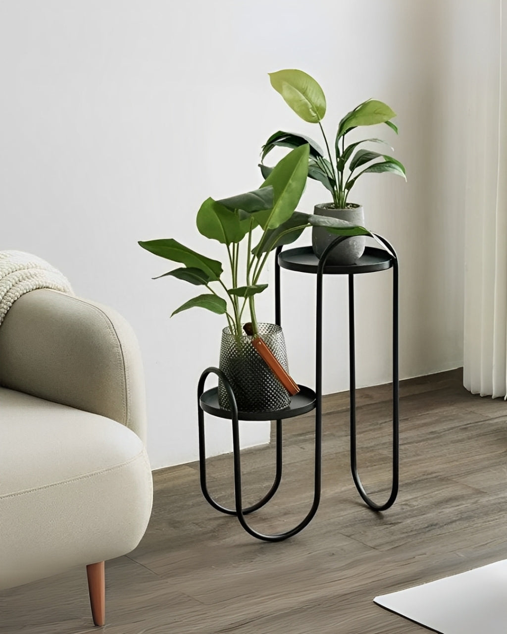 Modern black metal plant shelf with a thin, curved frame. The shelf has two tiers: a small round shelf on the right and a taller rectangular shelf on the left.