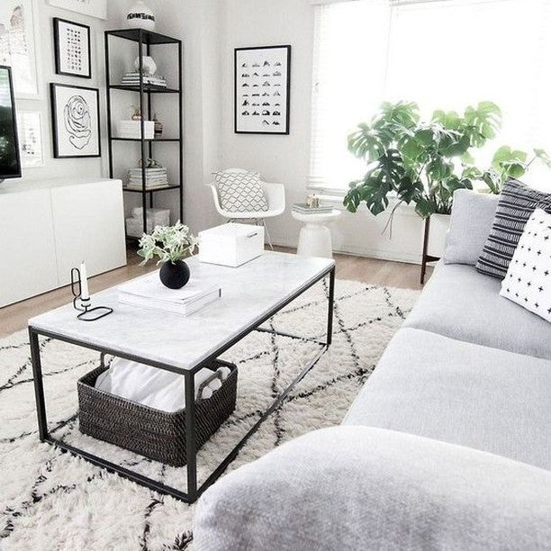 A rectangular coffee table with a white marble top and a black metal frame, situated in a bright living room.