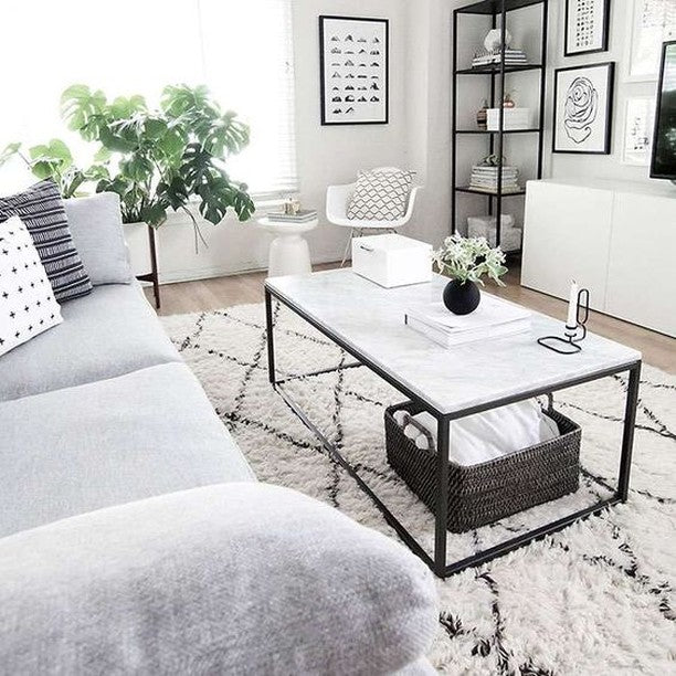 A rectangular coffee table with a white marble top and a black metal frame, situated in a bright living room.