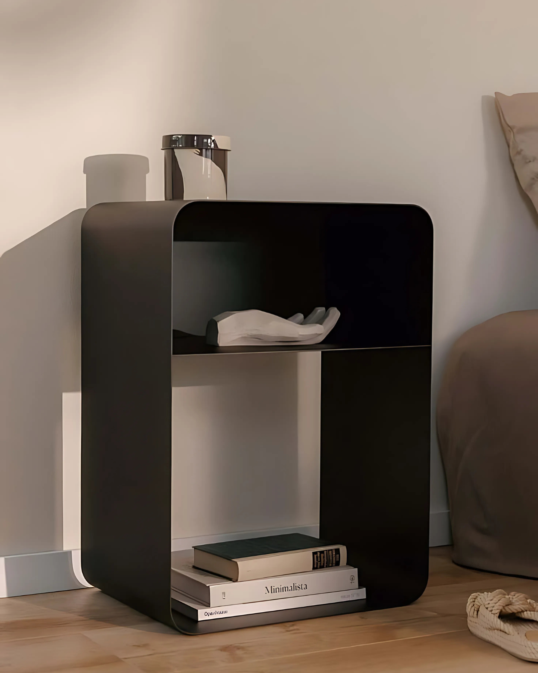 A clean and contemporary bedroom scene featuring a white, two-tiered cubic side table next to a bed. The table holds books and a glass, emphasizing its functionality and minimalist design.
