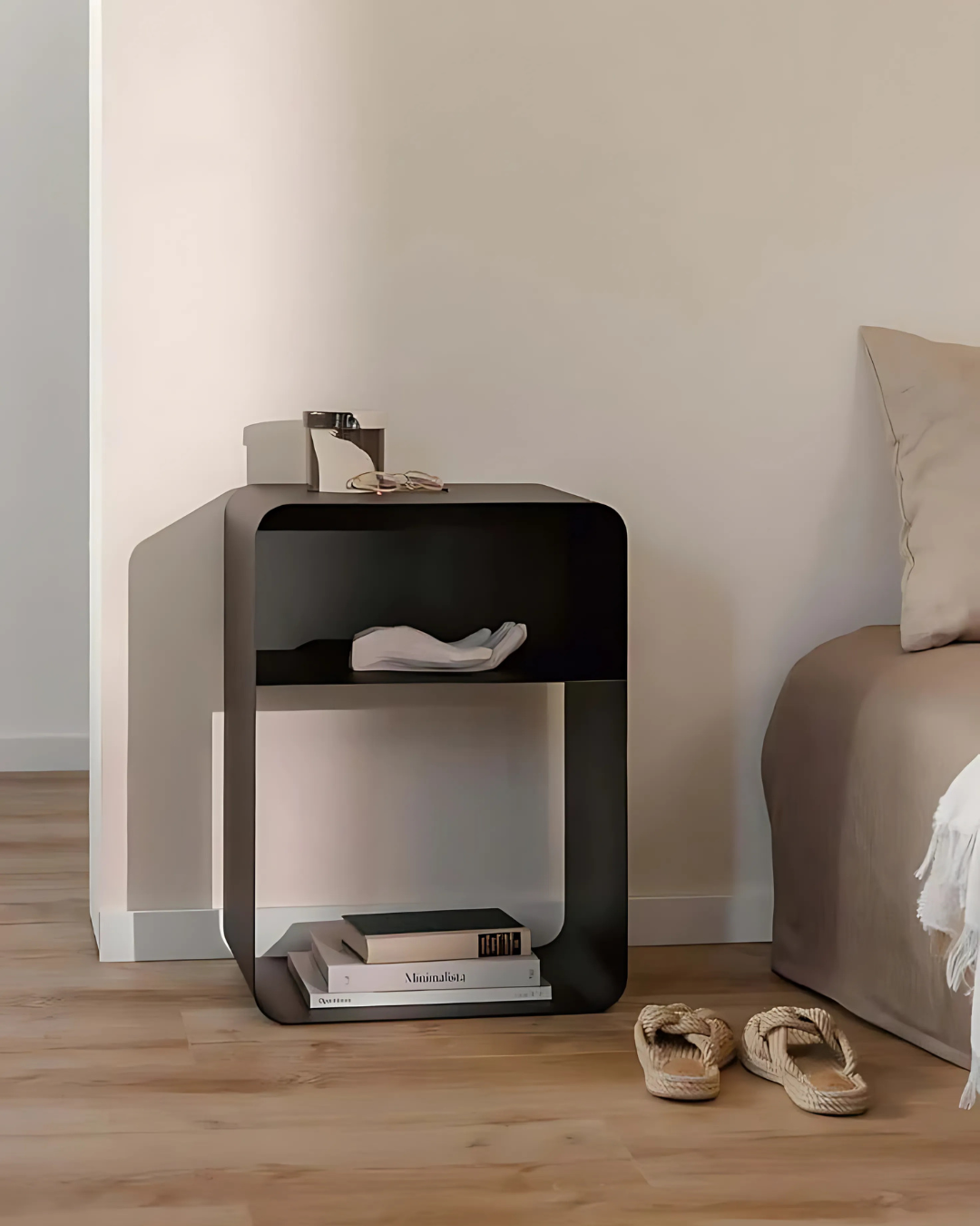 A clean and contemporary bedroom scene featuring a white, two-tiered cubic side table next to a bed. The table holds books and a glass, emphasizing its functionality and minimalist design.