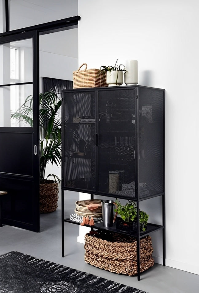 Black metal cabinet with mesh doors, displaying storage items and plants. Modern industrial style for home organization in Lebanon. Woven baskets and plants visible on top and bottom shelves.