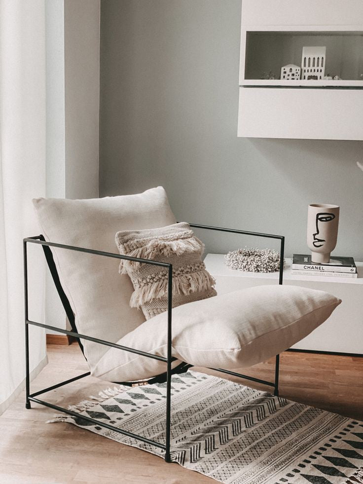 Contemporary living room furniture: black metal frame armchair with cream linen cushions, textured fringe pillow, and black and white patterned rug