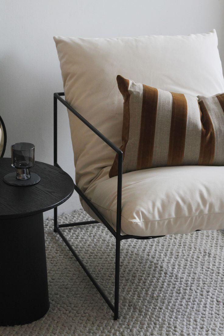 Contemporary living room furniture: black metal frame armchair with cream linen cushions, textured fringe pillow, and black and white patterned rug
