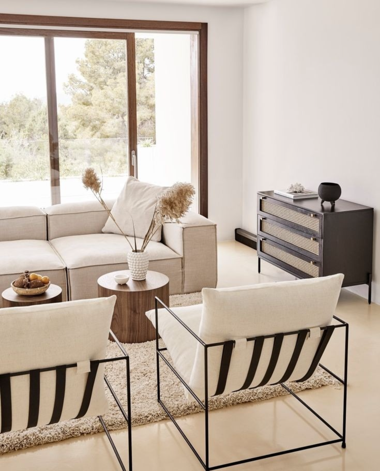 Contemporary living room furniture: black metal frame armchair with cream linen cushions, textured fringe pillow, and black and white patterned rug