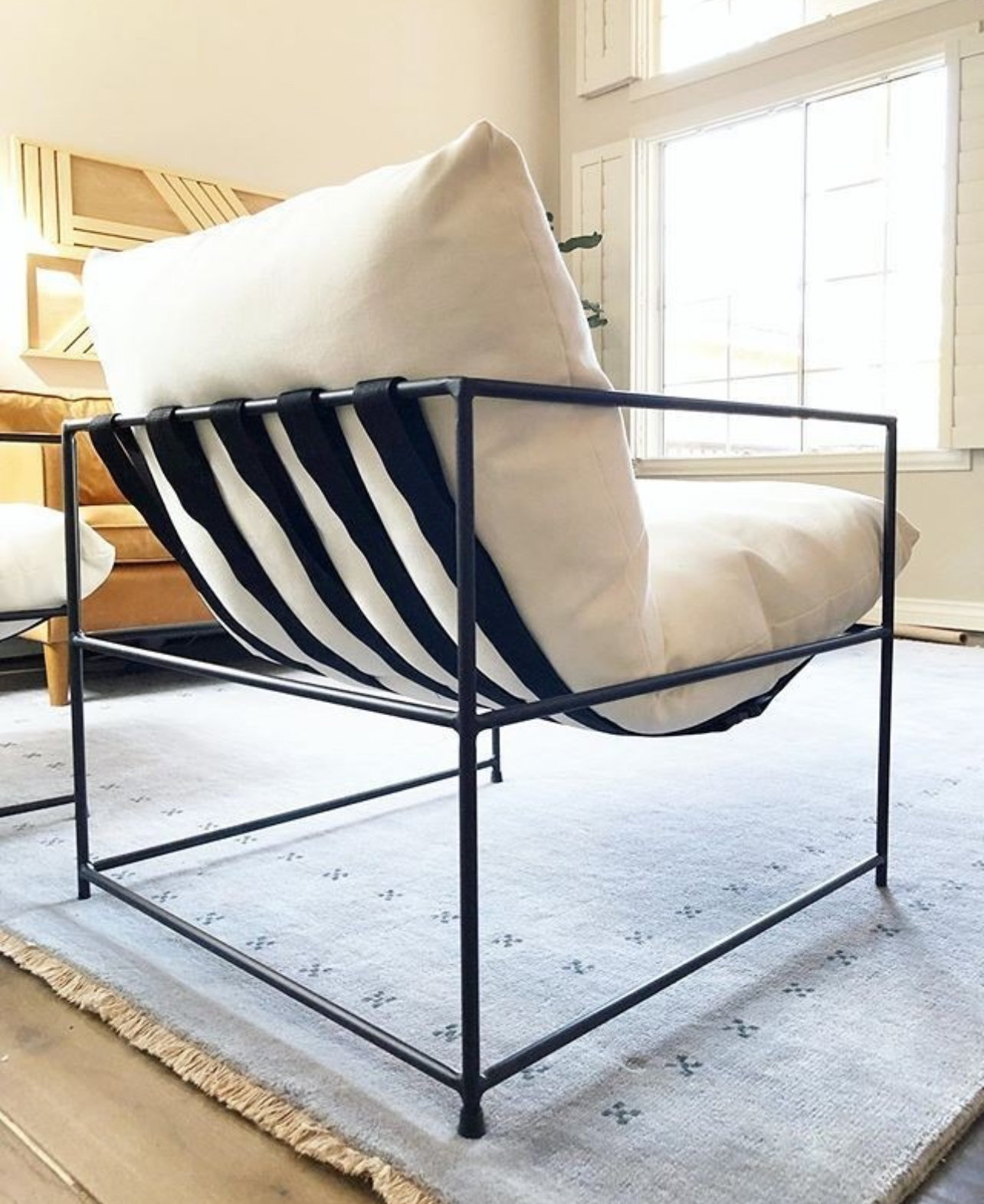 Contemporary living room furniture: black metal frame armchair with cream linen cushions, textured fringe pillow, and black and white patterned rug