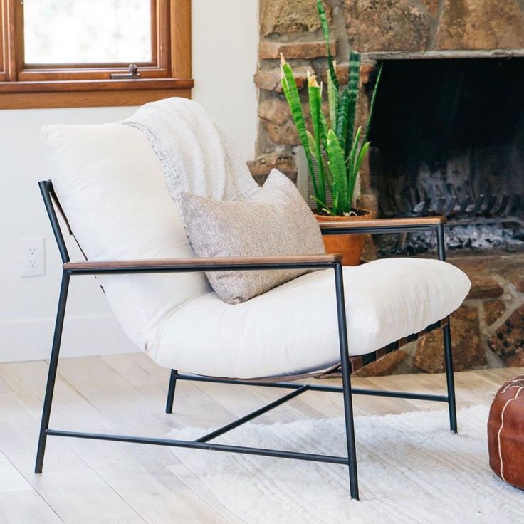 Contemporary armchair with beige cushions and black metal frame, striped brown pillow, and small round black side table with glass.