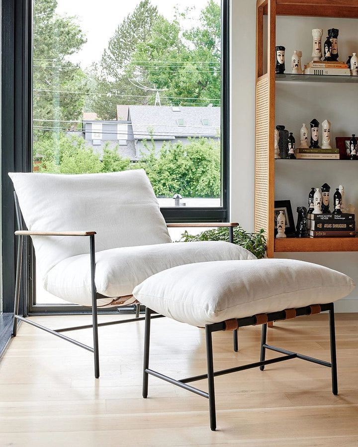 Contemporary armchair with beige cushions and black metal frame, striped brown pillow, and small round black side table with glass.
