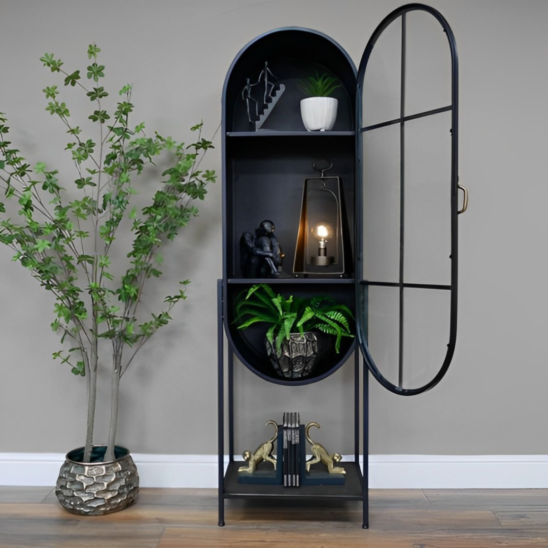Large industrial retro black metal oval display cabinet with glass door, showcasing decorative items. Unique vintage-inspired storage for homes in Lebanon. Open glass door and potted plant visible.