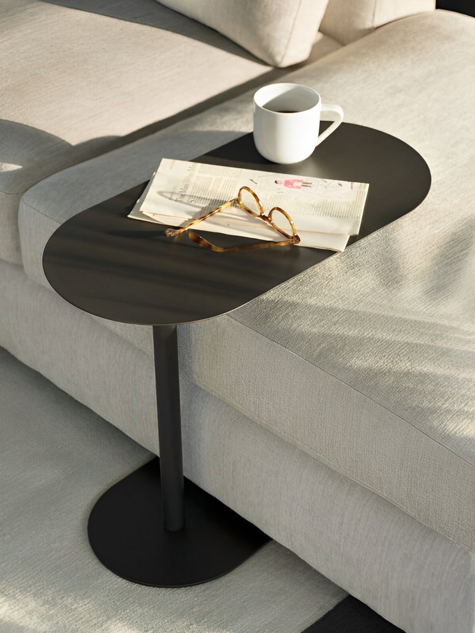 Contemporary black C-shaped side table with an oval top, positioned over a sofa.
