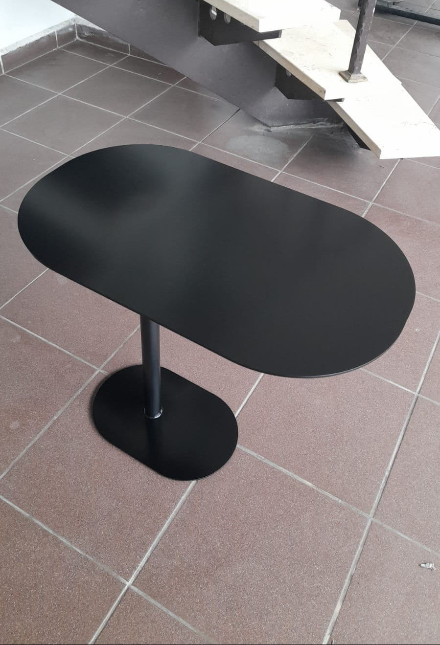 Contemporary black C-shaped side table with an oval top, positioned over a sofa.