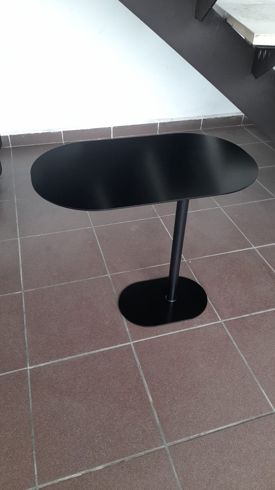 Contemporary black C-shaped side table with an oval top, positioned over a sofa.