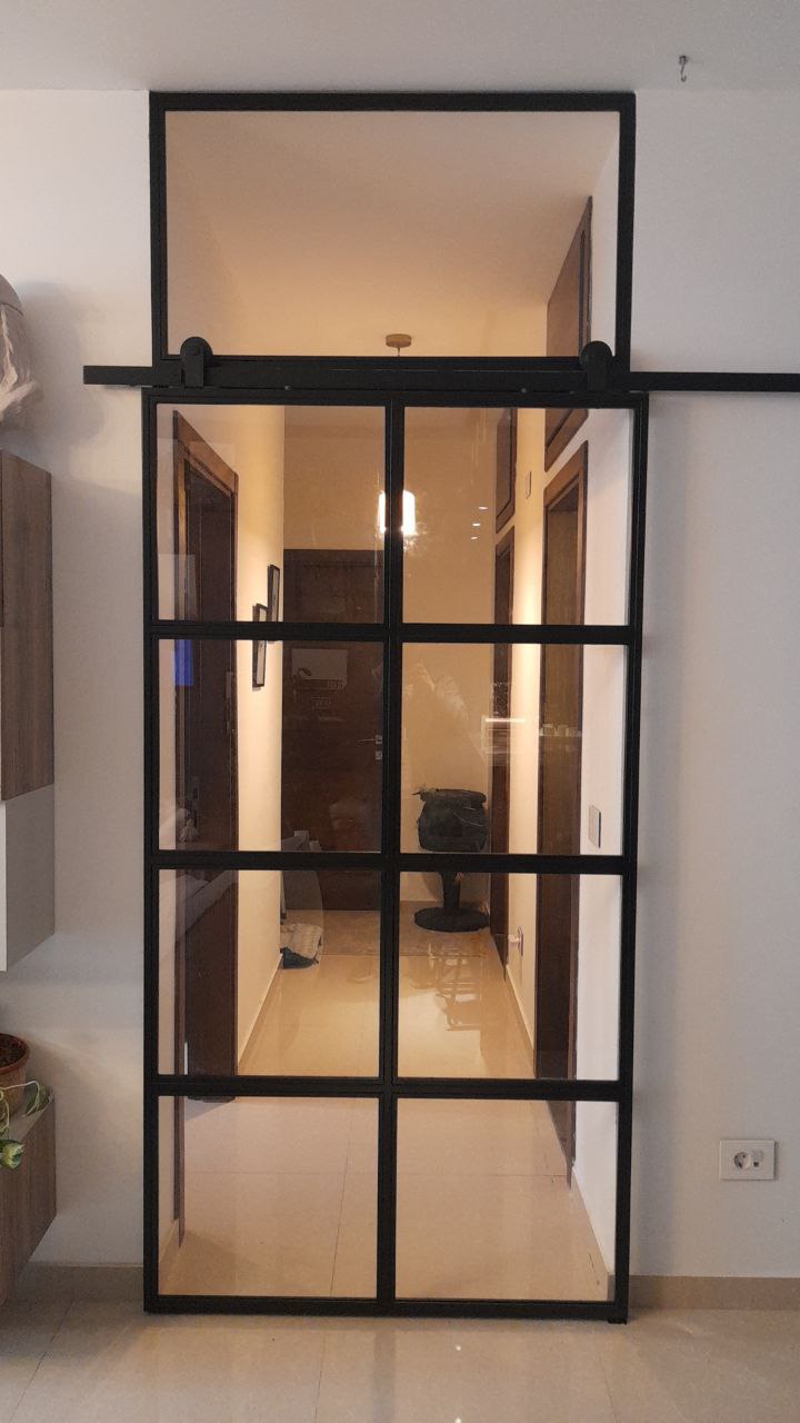 Modern glass sliding door with black metal framing and frosted panels, mounted on a black track