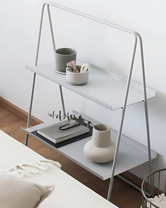 A minimalist light gray A-Table leans against a white wall, showcasing its simple and elegant design. The table features two rectangular shelves supported by an A-shaped frame made of slender, rounded metal. Its open structure and clean lines create a light and airy feel.