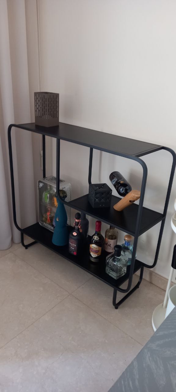 The Alana console, a black metal table with shelves, showing a vase, books, and a speaker.