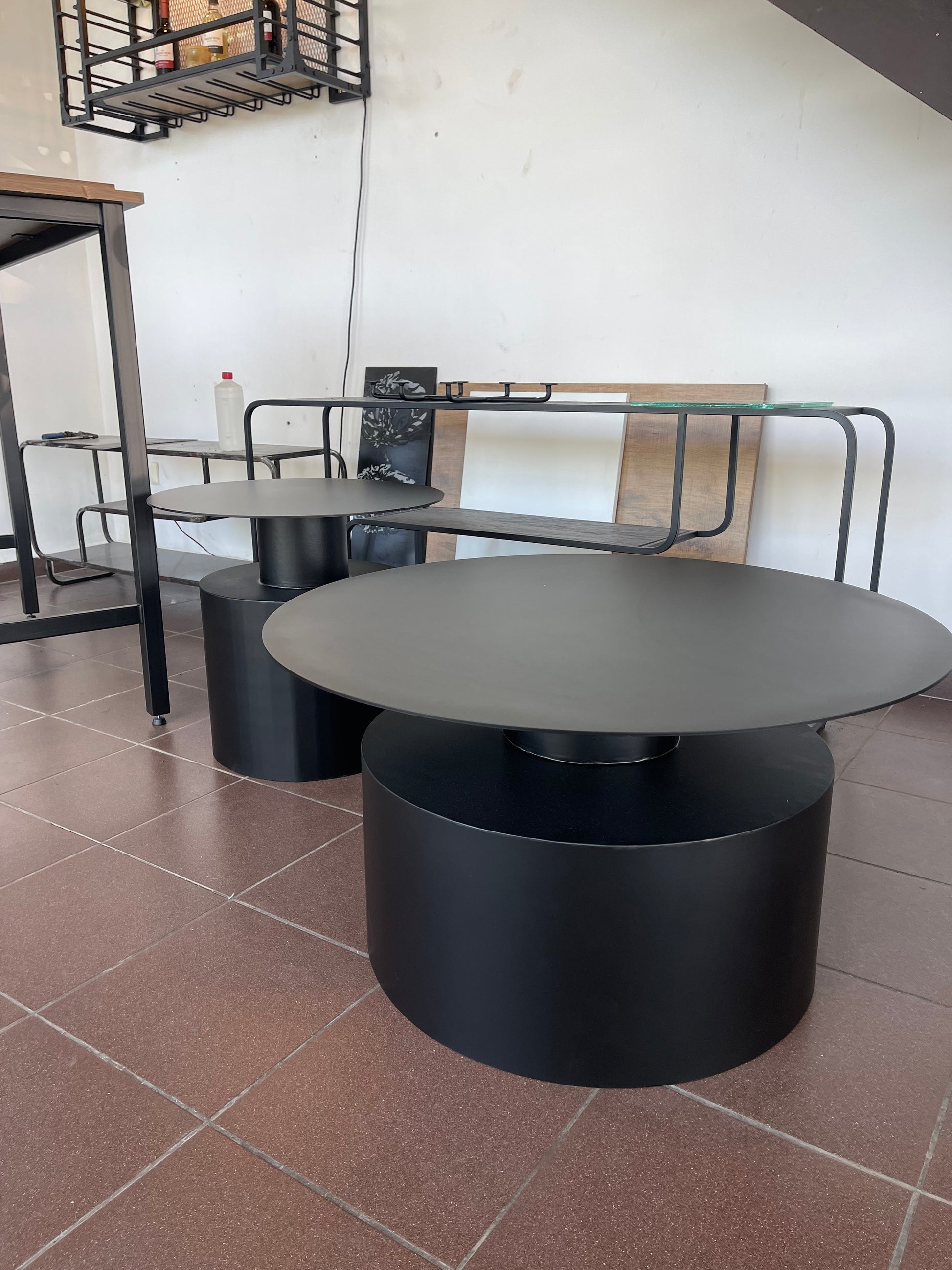 Modern nesting coffee tables with geometric shapes, featuring black metal oval and round tops and cylindrical bases.